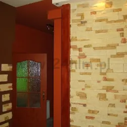 Dekoracyjna ściana z kamienia elewacyjnego w odcieniach beżu i brązu, sąsiadująca z pomarańczową ścianą i drewnianą ościeżnicą drzwi z szybą.