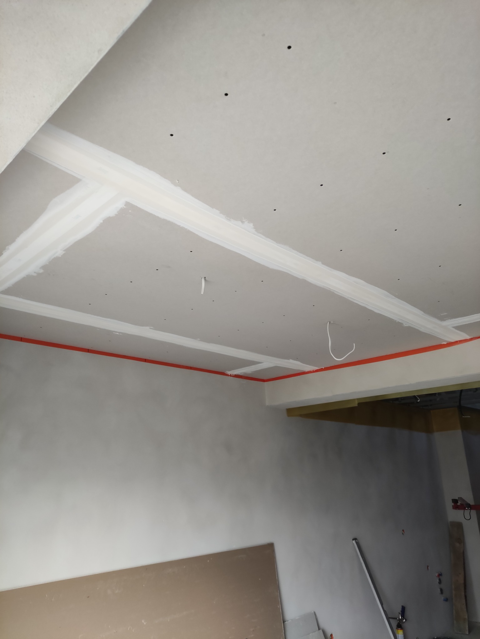 Sufit z płyt kartonowo-gipsowych w trakcie montażu, widoczne łączenia zaszpachlowane, czerwone rurki instalacji elektrycznej, widok z dołu.