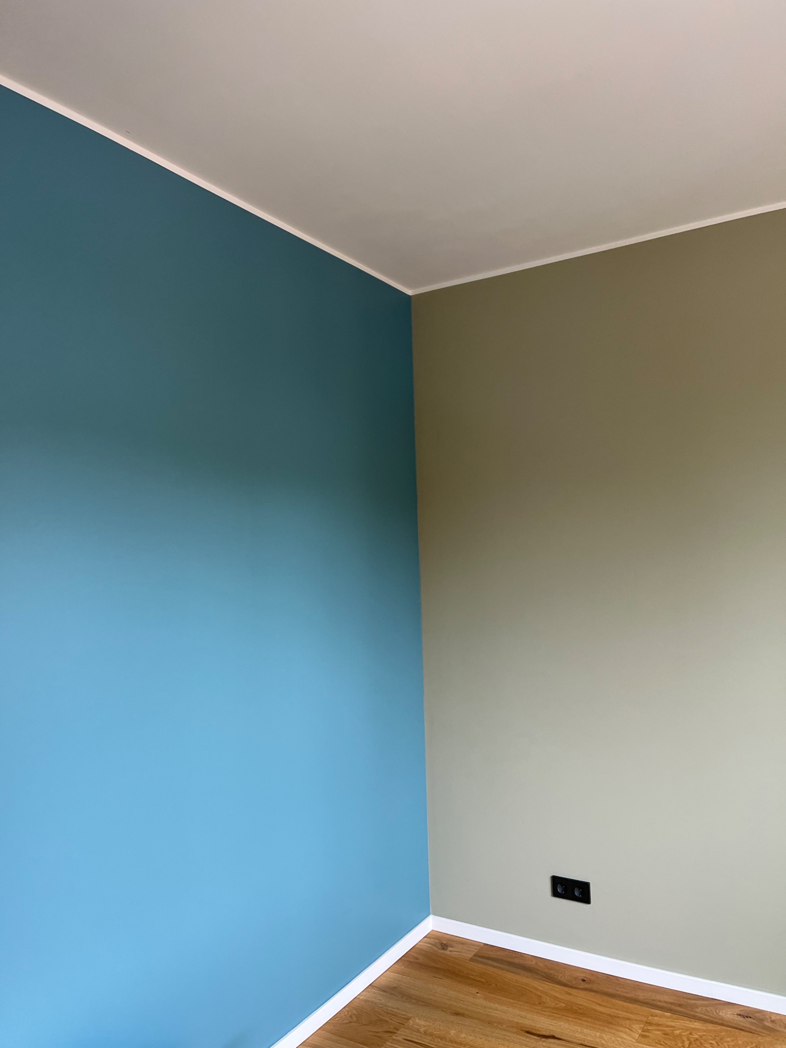 Ściana pomalowana na dwa kolory w Puławach: błękitny i oliwkowy. Widoczna podłoga z paneli i biała listwa przypodłogowa. Kontrastowe barwy ścian.