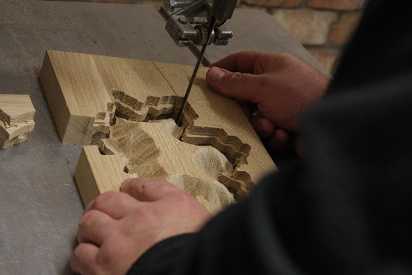 Precyzyjne wycinanie kształtu w jasnym drewnie za pomocą piły włosowej, fragmenty oddzielone, widoczne słoje drewna.