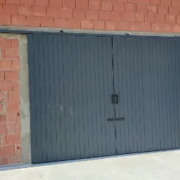 Zamknięta, szara brama przesuwna z pionowymi panelami i czarnymi uchwytami na tle surowej, czerwonej cegły z widocznym mechanizmem przesuwnym.