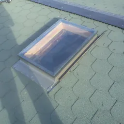 Zielony dach pokryty gontem bitumicznym z zamontowanym oknem dachowym i elementami wentylacyjnymi w górnej części.