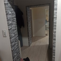 KAZDY SZCZEGÓŁ DOPRACOWANY - Wykończone przejście między pokojami w Legnicy, obłożone tapetą imitującą kamień, widoczne buty przy ścianie i fragment garderoby w tle.