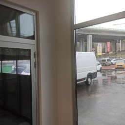 KAZDY SZCZEGÓŁ DOPRACOWANY - Wnętrze biura z widokiem na deszczowy parking i białą furgonetkę przez duże okno.