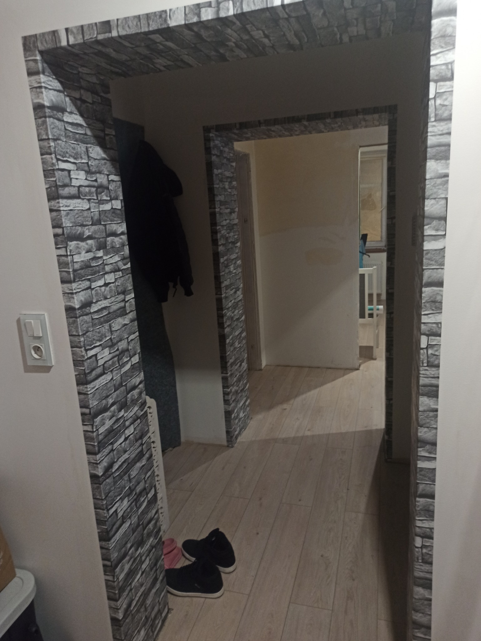 Wykończone przejście między pokojami w Legnicy, obłożone tapetą imitującą kamień, widoczne buty przy ścianie i fragment garderoby w tle.