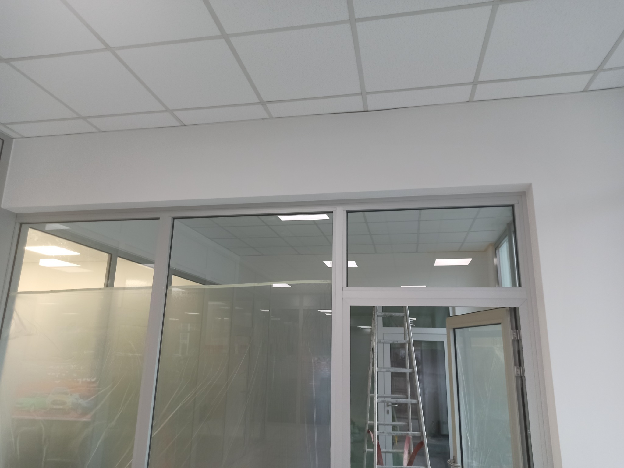 Biuro z nowym sufitem kasetonowym i przeszklonymi ścianami, zabezpieczonymi folią malarską, drabina oparta o ścianę.