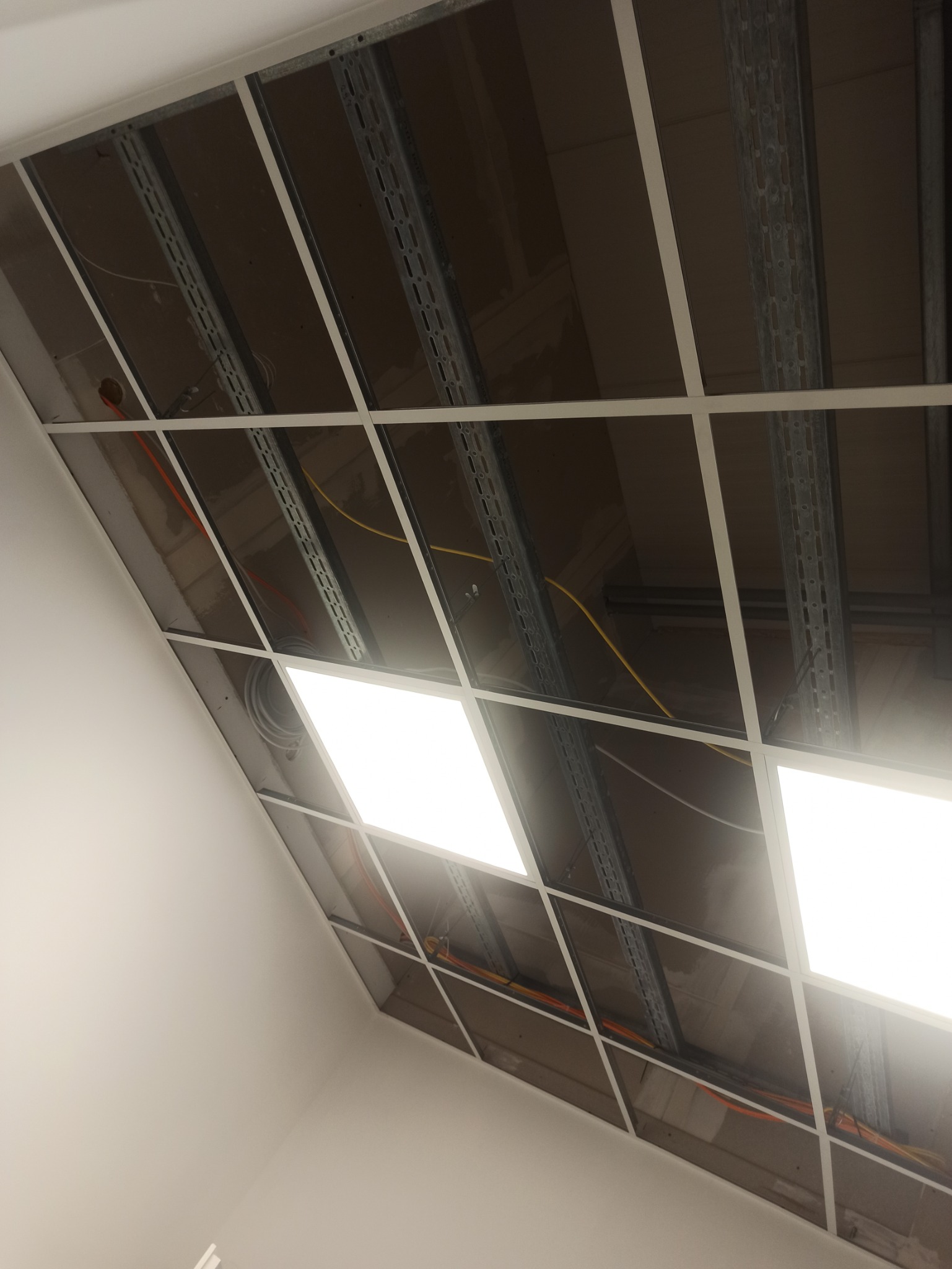 Montaż sufitu podwieszanego z widoczną konstrukcją nośną, instalacją elektryczną i panelami oświetleniowymi.