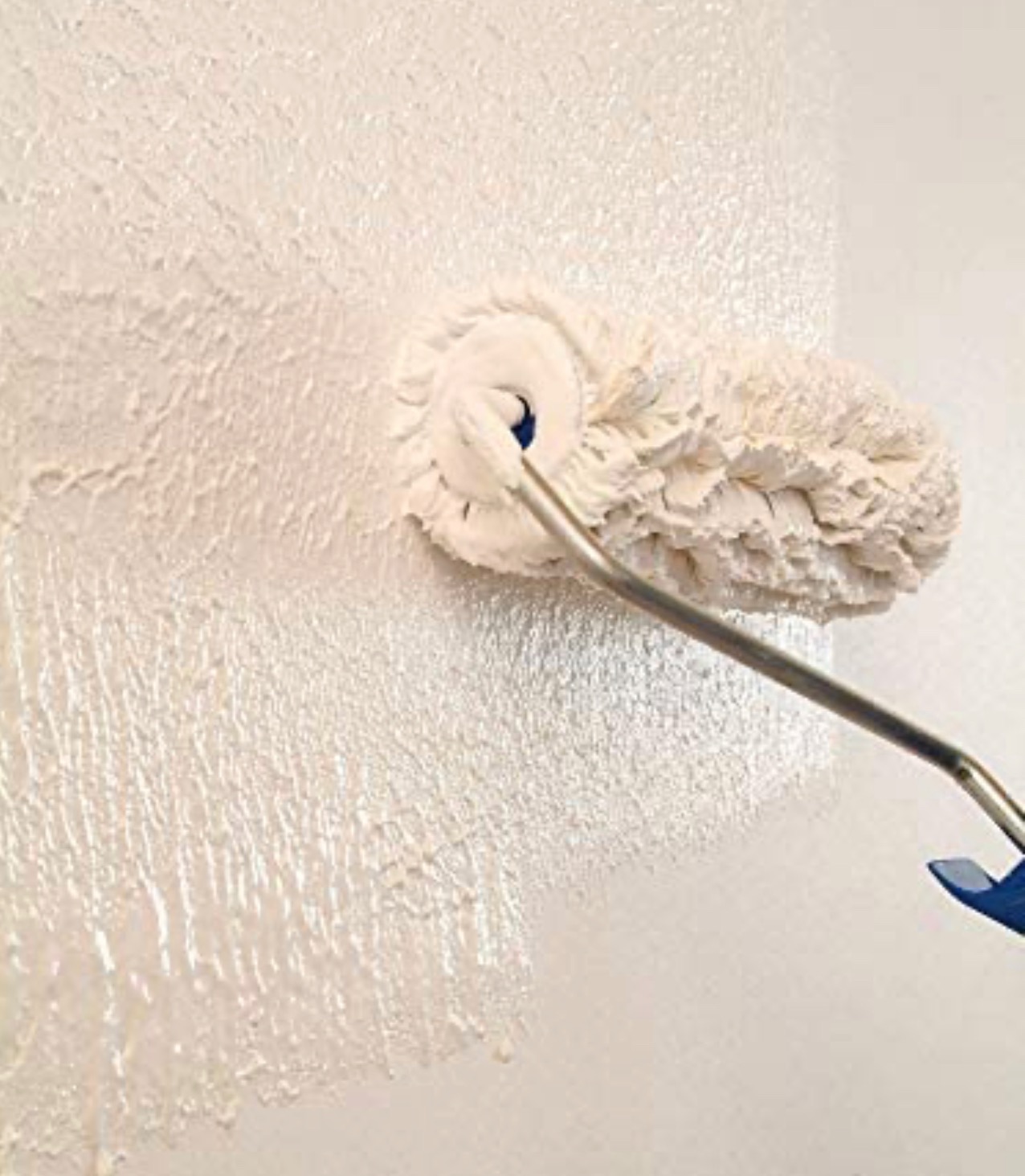 Wałek malarski z długą rączką, nakładający świeżą, białą farbę na ścianę, tworząc widoczną fakturę.