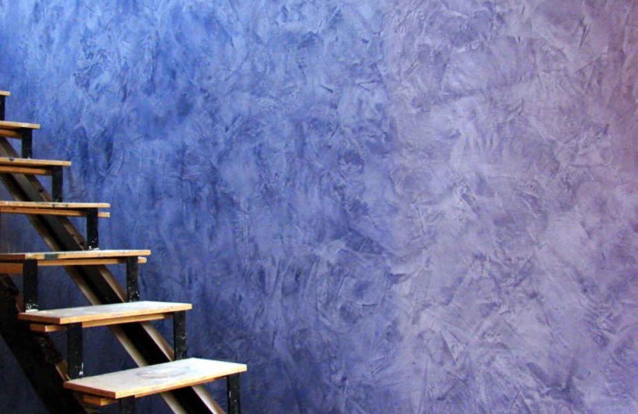 Ściana z dekoracyjną fakturą w odcieniach fioletu i błękitu, widoczne drewniane schody z metalowymi elementami.