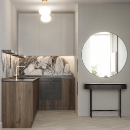 DESIGN ME Studio - Kompaktowa kuchnia z marmurowym blatem i okrągłym lustrem. Drewniane szafki dolne kontrastują z jasnymi górnymi. Złota bateria i lampa dodają elegancji.