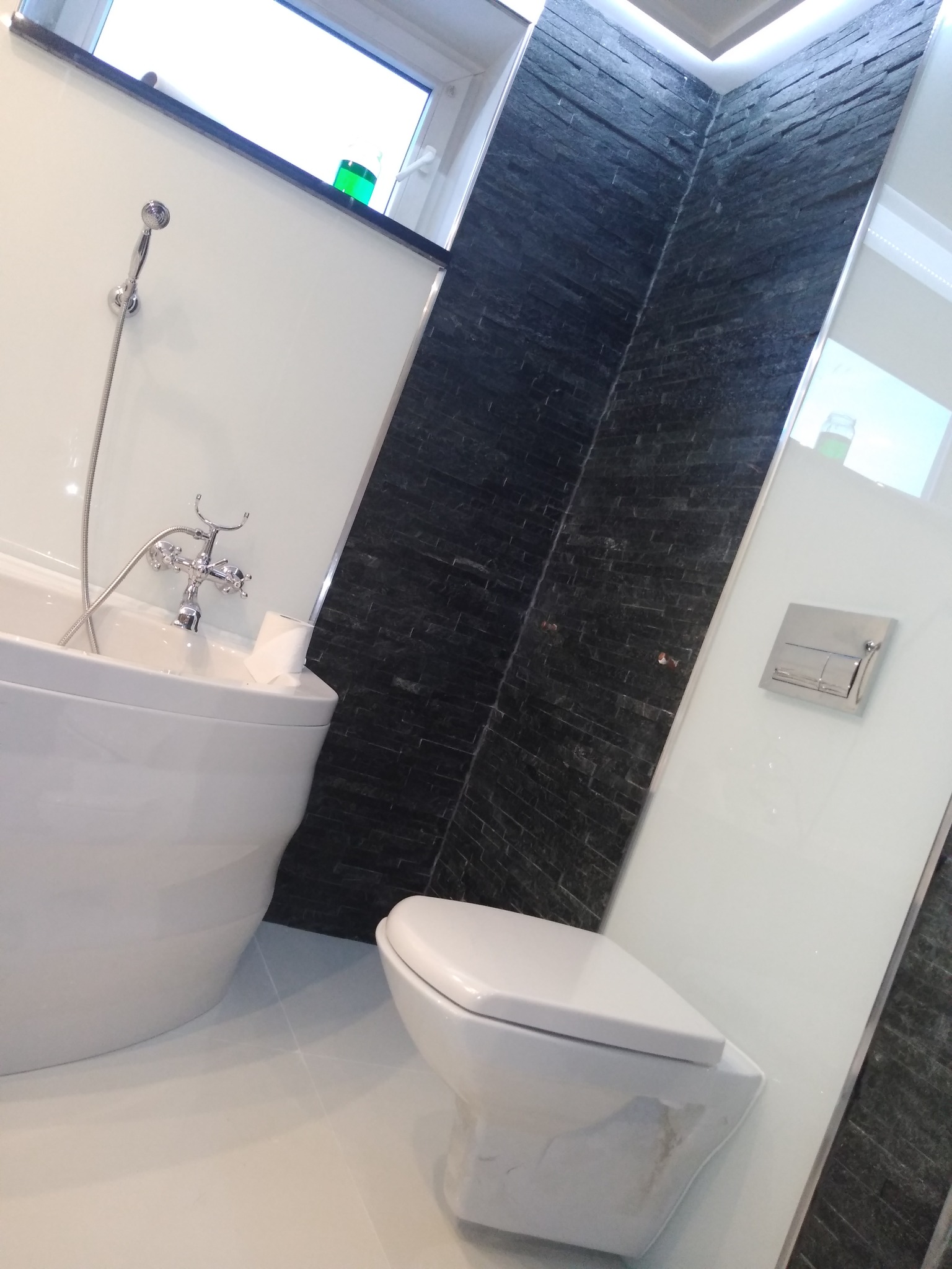 Nowoczesna łazienka z białą wolnostojącą wanną, toaletą i ścianą wyłożoną czarnym kamieniem, oświetlona ledowym światłem.