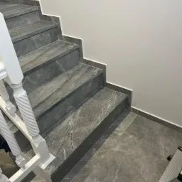 Schody wyłożone szarym marmurem z białymi, ozdobnymi balustradami i fragmentem drabiny w rogu.