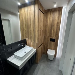 Żakard Meble - Nowoczesna łazienka w Nowym Opolu z drewnianą zabudową, umywalką nablatową na czarno-białym postumencie i podświetleniem LED, widok z perspektywy kabiny prysznicowej.