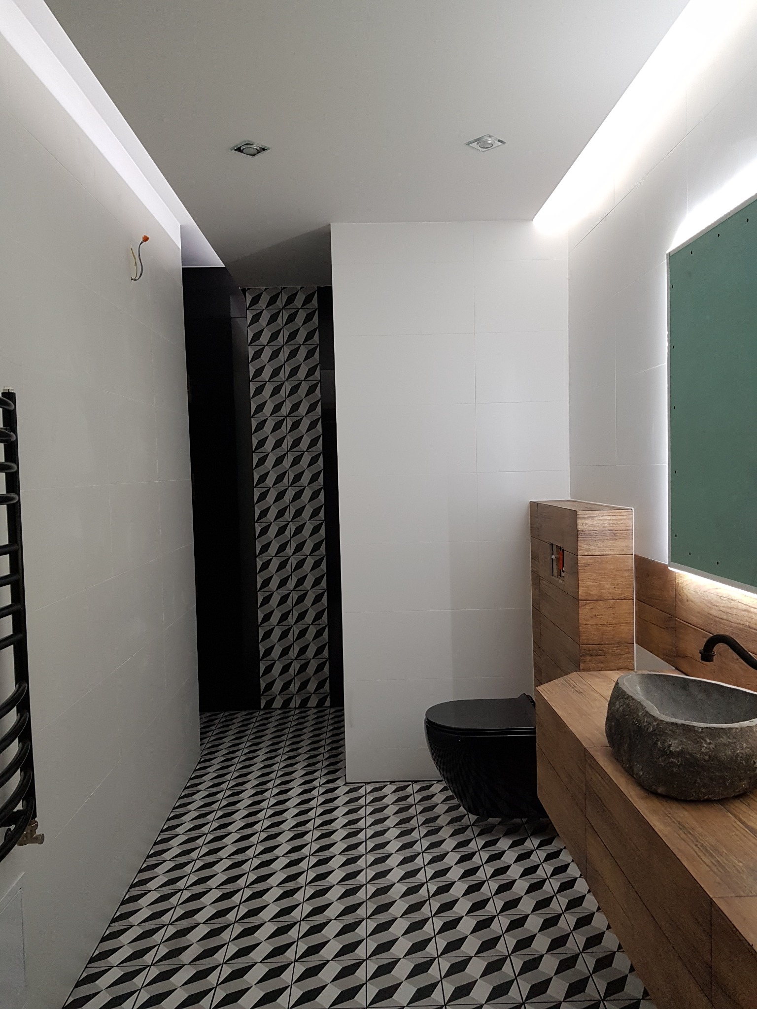 Nowoczesna łazienka z czarną armaturą, umywalką z kamienia i geometrycznymi płytkami podłogowymi w odcieniach szarości i czerni, oświetlona listwami LED.