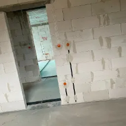 Surowy stan budynku: Widok na ścianę z betonu komórkowego z wywierconymi otworami i poprowadzonymi przewodami elektrycznymi, widoczne puszki instalacyjne i kable, napis 'TERM.' na ścianie...