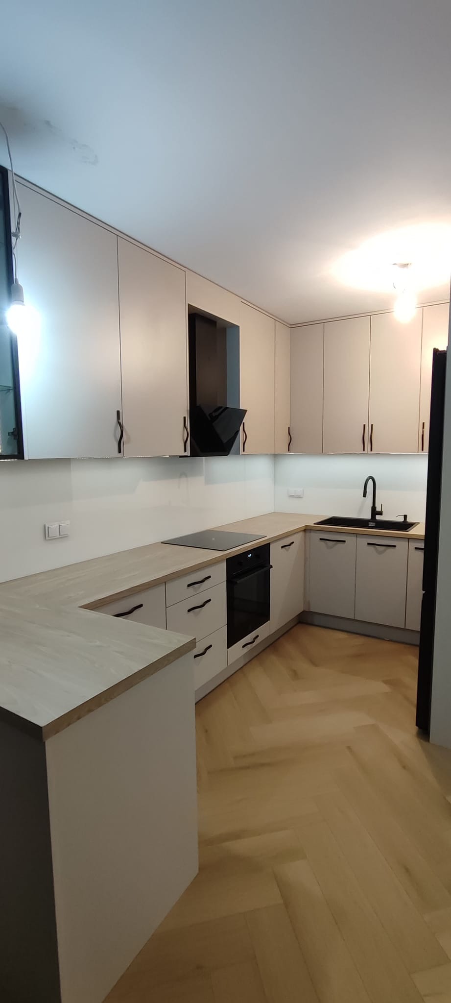 Jasna kuchnia z drewnianym blatem, czarną armaturą i sprzętem AGD, oraz podłogą ułożoną w jodełkę.