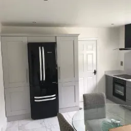 Nowoczesna kuchnia w odcieniach szarości i bieli z czarną lodówką i okapem, marmurowe płytki podłogowe i szklany stół jadalny.