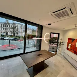 Nowoczesne biuro z dużym oknem, przez które widać budynek sądu, minimalistyczny stół konferencyjny i okrągła lampa sufitowa.