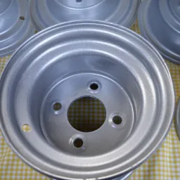 Srebrne felgi aluminiowe po renowacji, leżące na żółto-białej kraciastej tkaninie, widoczne ślady obróbki.