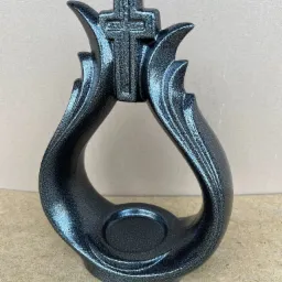 Metalowa, czarna, błyszcząca ozdoba z krzyżem na górze, na brązowym tle.