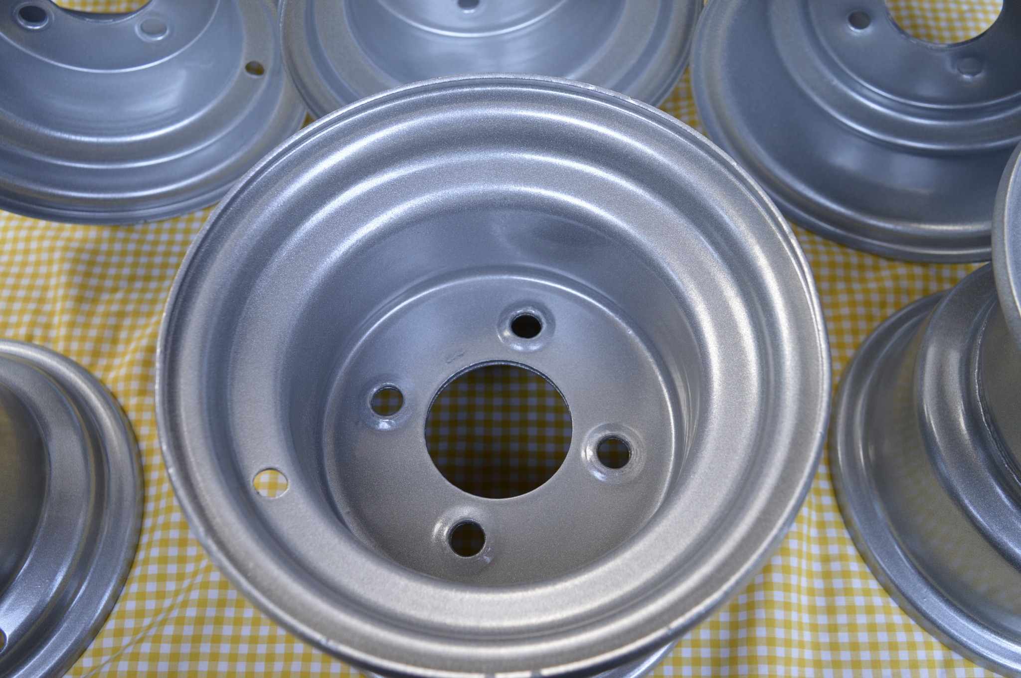 Srebrne felgi aluminiowe po renowacji, leżące na żółto-białej kraciastej tkaninie, widoczne ślady obróbki.