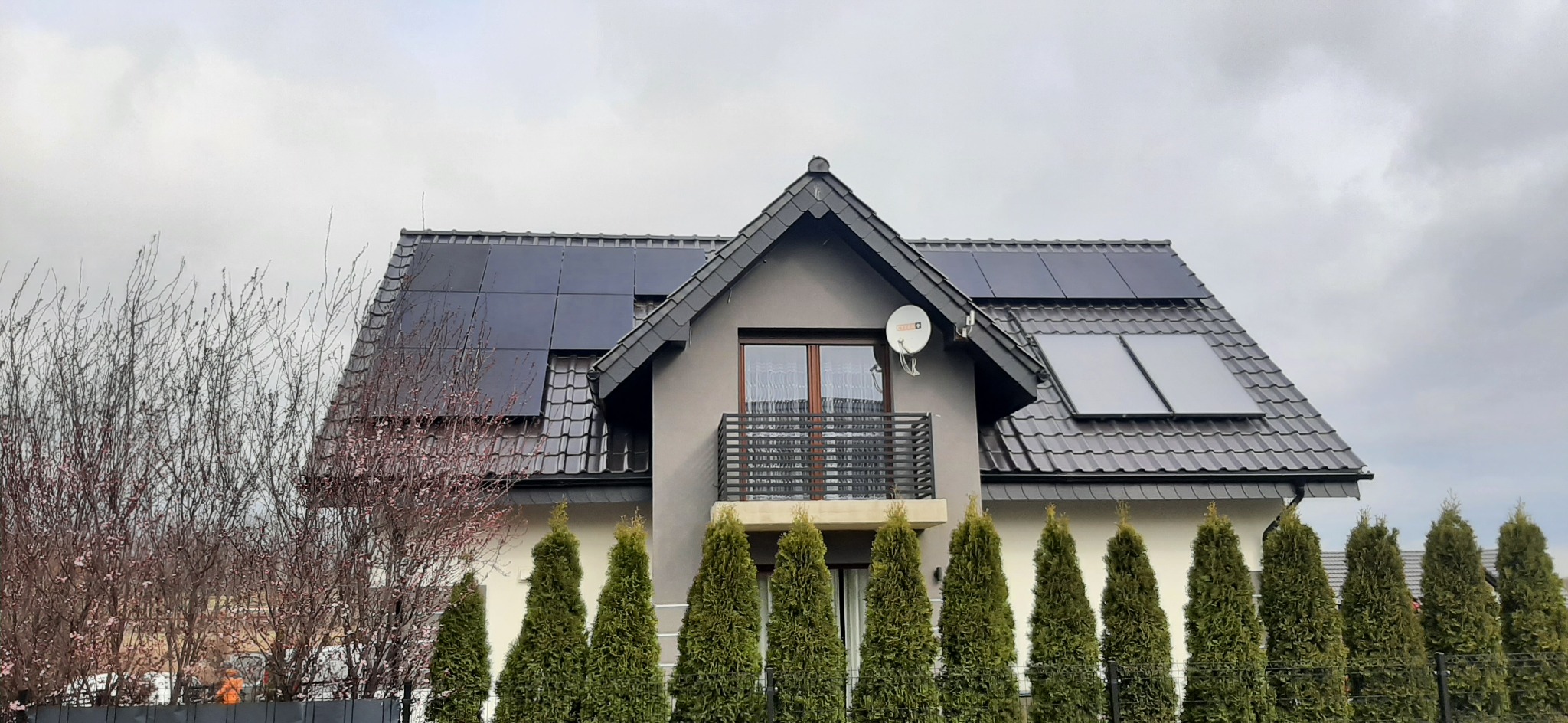Dom jednorodzinny z zamontowanymi panelami słonecznymi na dachu, widok z przodu, pochmurne niebo w tle.