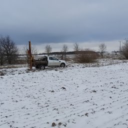 MIKA-GEO Geologia Michał Kacprzak - Prace geologiczne w zimowej scenerii Zielonki. Biały samochód terenowy z wiertnicą na zasypanym śniegiem polu. Pochmurne niebo.