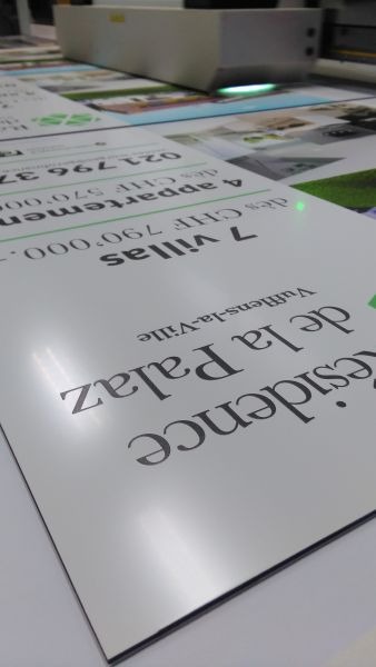 Proces druku wielkoformatowego: arkusze z nadrukiem 'Residence de la Palaz Vufflens-la-Ville, 7 Villas, 4 appartements' na białym podłożu pod głowicą drukarki.