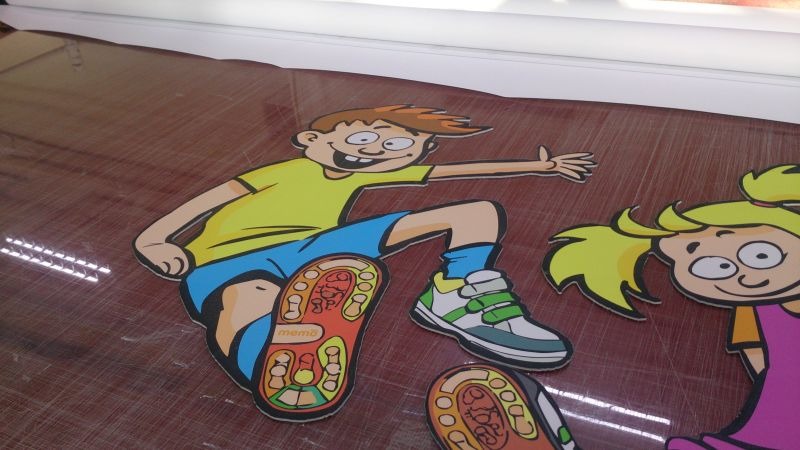 Wycięte z folii postacie dzieci, chłopiec i dziewczynka, z widocznymi detalami podeszw butów, ułożone na brązowym podłożu.