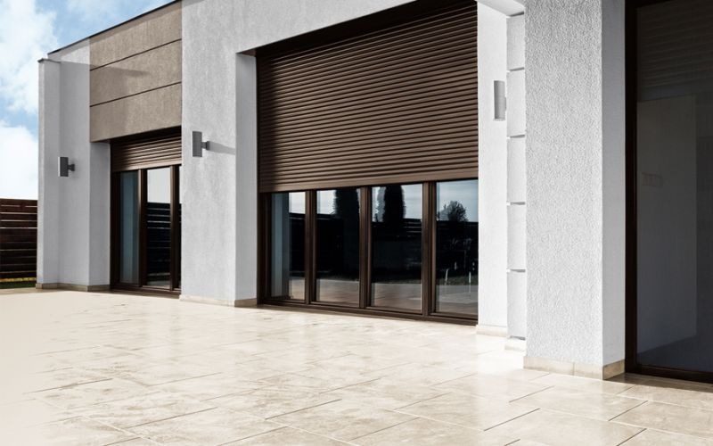 Brązowe rolety zewnętrzne na oknach w domu jednorodzinnym w Żywcu, widok z zewnątrz na jasny taras.