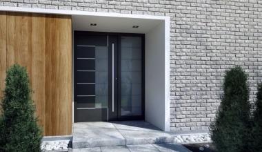 Nowoczesne wejście do domu z czarnymi drzwiami z przeszkleniami, obok drewniana okładzina ściany i fragment elewacji z jasnej cegły.