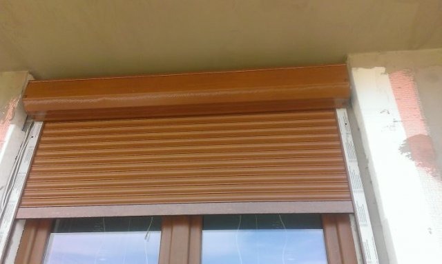Brązowa roleta zewnętrzna, częściowo opuszczona, zamontowana w oknie; widoczna surowa ściana po remoncie.