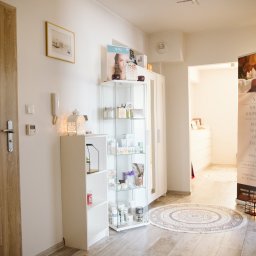 Czas Relaksu Tomasz Marciniak - Jasne wnętrze gabinetu z przeszkloną witryną pełną kosmetyków, dekoracyjnymi lampionami i banerem reklamowym z ofertą masaży terapeutycznych.