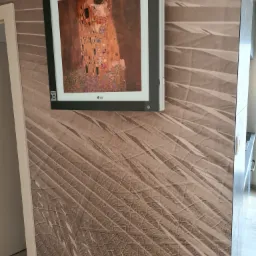 Klimatyzator LG z obrazem Gustava Klimta 'Pocałunek' na ścianie z wzorem liści palmowych.