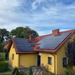 Żółty dom jednorodzinny w Krakowie z czerwoną dachówką i panelami słonecznymi na dachu, widok z góry, błękitne niebo z chmurami w tle.