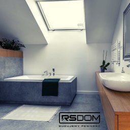 www.rs-dom.pl - Usługi budowlane, remonty, wykończenia wnętrz, budowa domów - Nowoczesna łazienka na poddaszu z oknami dachowymi: wanna obudowana szarą płytką, podwieszana toaleta, umywalka nablatowa na drewnianym blacie, rośliny w donicach, szary dywanik i logo firmy RSDOM...