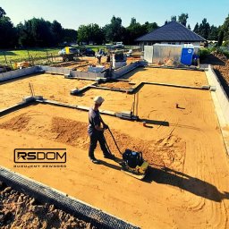 www.rs-dom.pl - Usługi budowlane, remonty, wykończenia wnętrz, budowa domów - Prace ziemne przy budowie fundamentów domu jednorodzinnego: ubijanie piasku zagęszczarką wewnątrz betonowych szalunków, widoczne zbrojenia i przygotowany teren pod wylewkę.