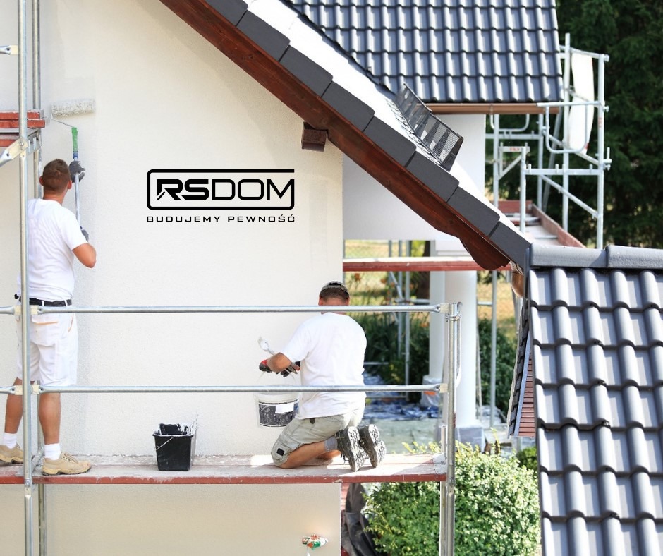 Dwóch malarzy na rusztowaniu maluje elewację domu jednorodzinnego na biało, widoczne logo firmy budowlanej RS Dom i fragment dachu z szarej dachówki.