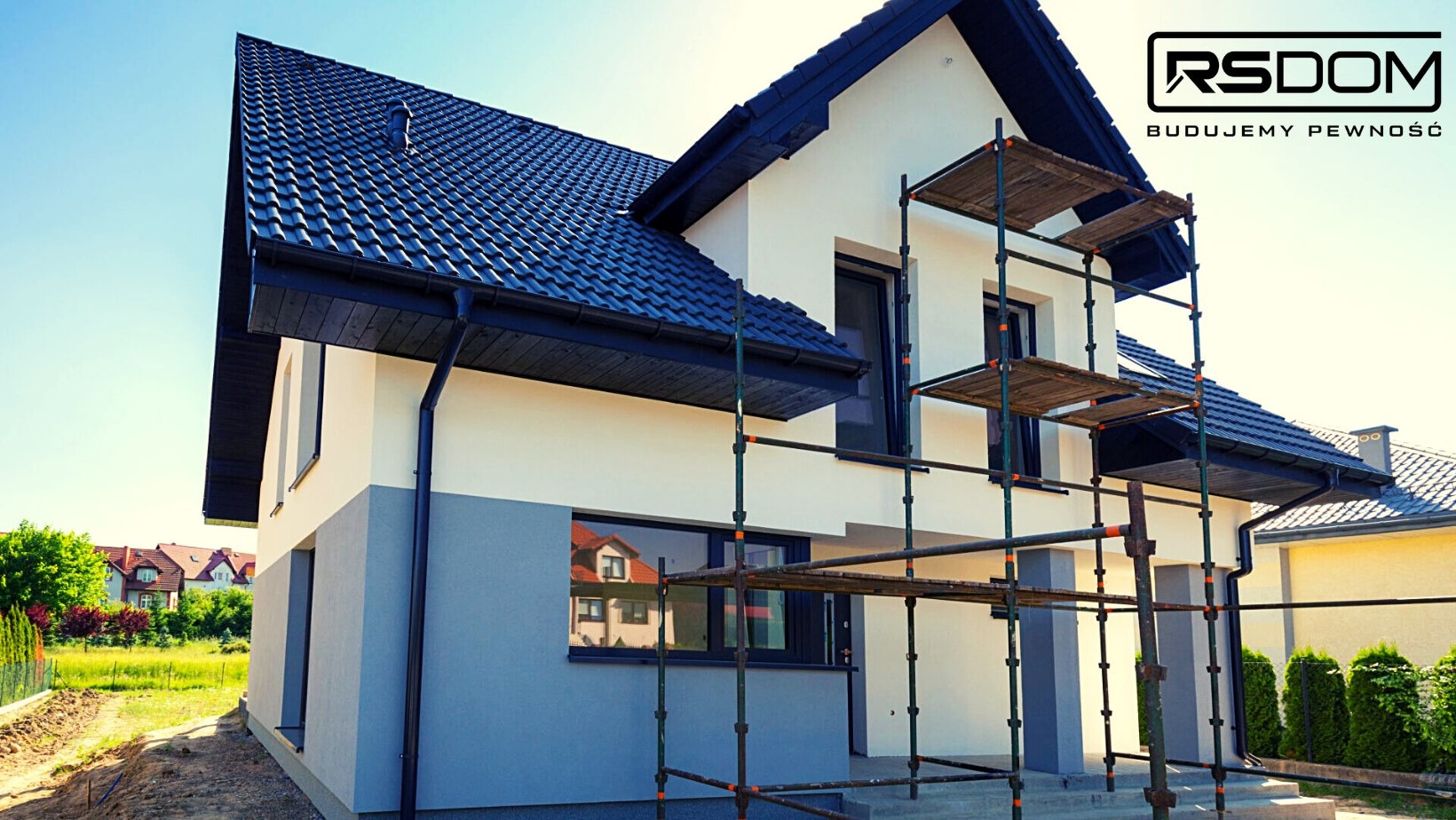 Dwukondygnacyjny dom z ciemną dachówką i rusztowaniem, widoczne logo firmy RS Dom