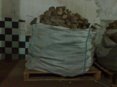 Worek z brykietem, ułożony na drewnianej palecie, w tle ściana z szachownicą z płytek.