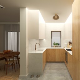 Coren Studio Design - Nowoczesna kuchnia z drewnianymi frontami, marmurowym blatem i miedzianą armaturą. Widok na jadalnię z okrągłym stołem i miskami dla zwierząt na podłodze.