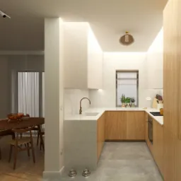 Nowoczesna kuchnia z drewnianymi frontami, marmurowym blatem i miedzianą armaturą. Widok na jadalnię z okrągłym stołem i miskami dla zwierząt na podłodze.