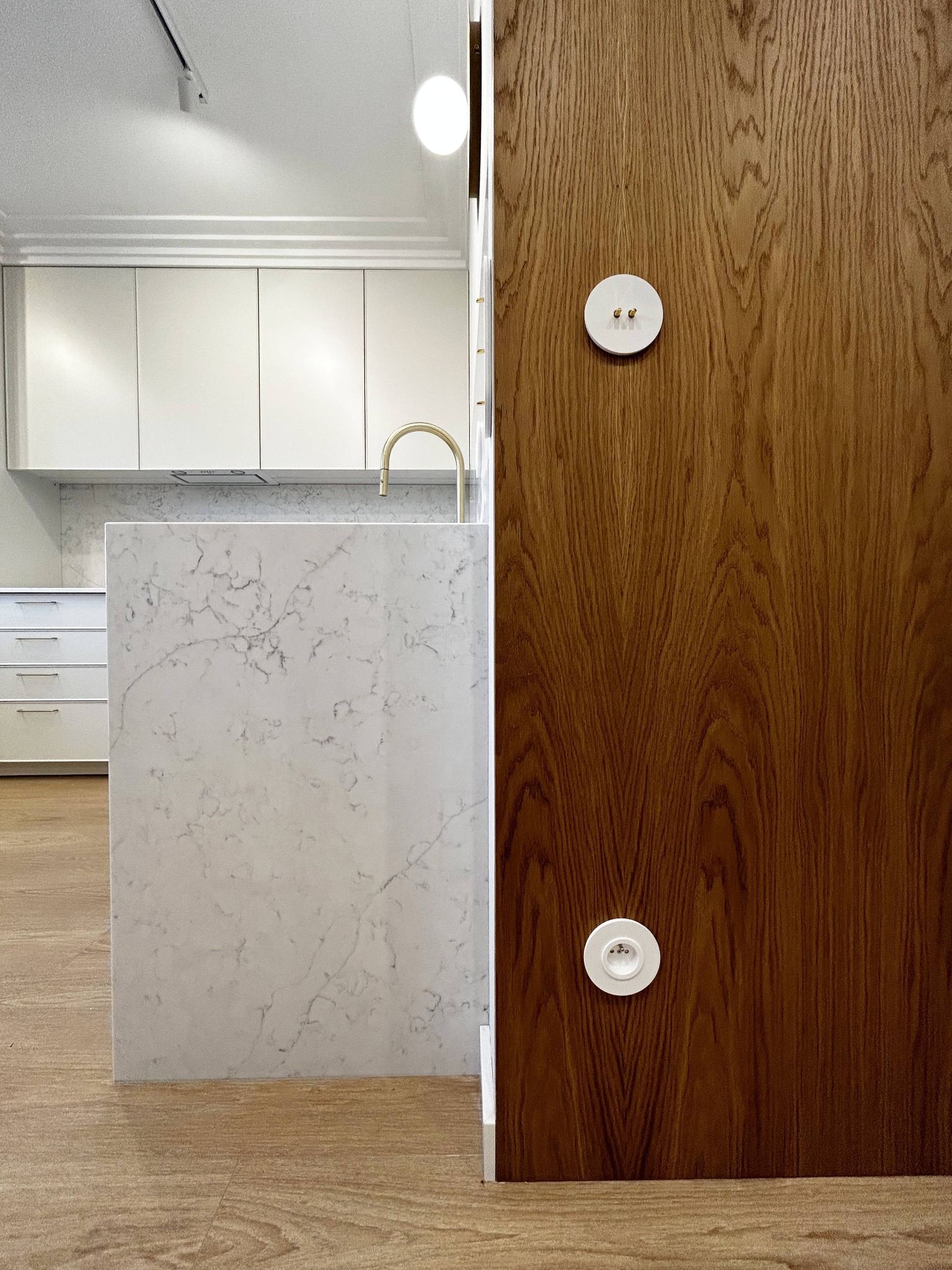 Kuchenna wyspa z marmurowym blatem i drewniana ściana z włącznikami w stylu retro, w jasnym wnętrzu. Widok na zabudowę kuchenną w tle.