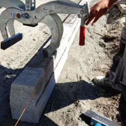 Precyzyjne układanie granitowych krawężników w Chorzowie przy użyciu chwytaka mechanicznego; widoczny sznurek traserski i gumowy młotek.