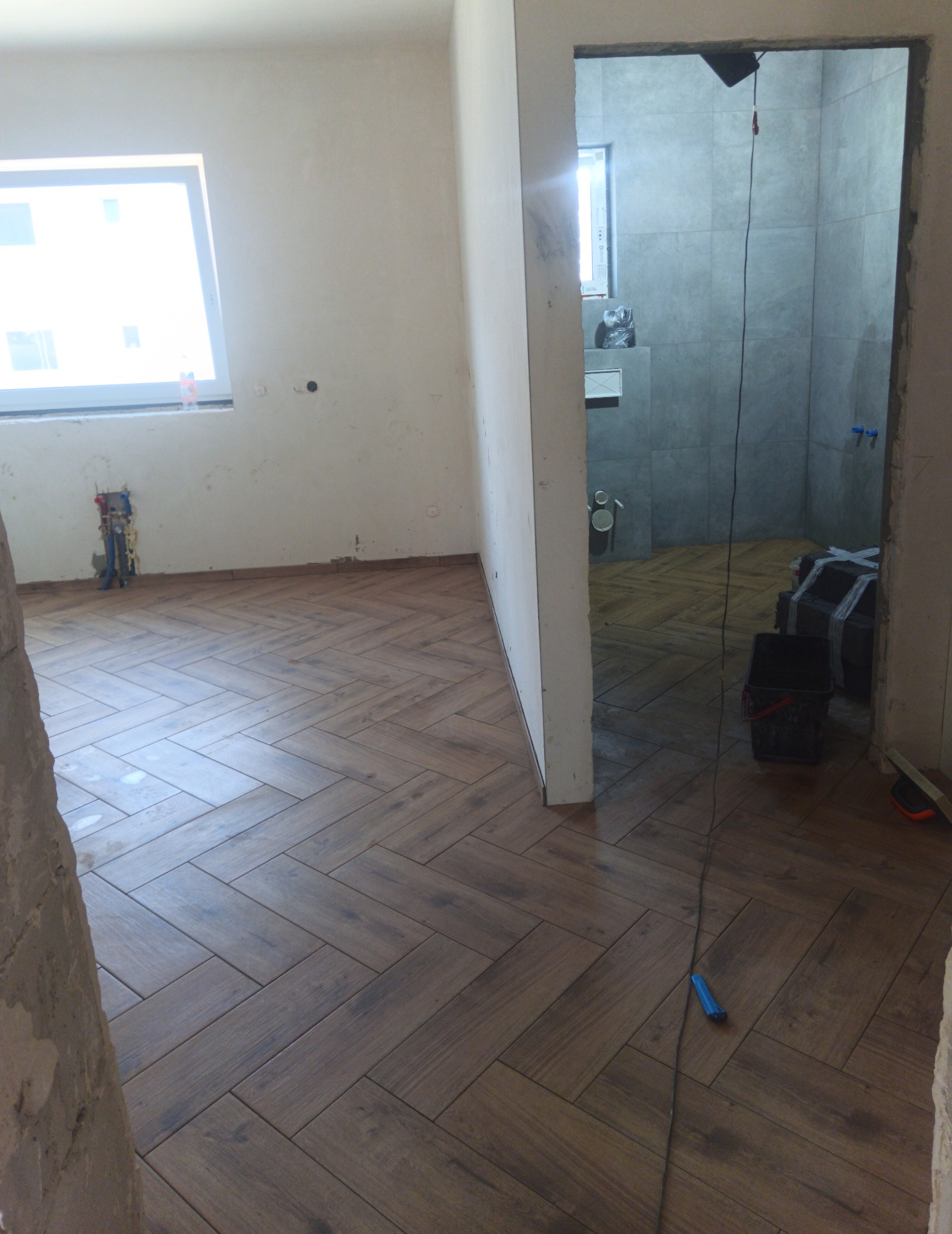 Układanie drewnopodobnych płytek w jodełkę w pokoju i łazience w trakcie remontu, widoczne narzędzia i instalacje.