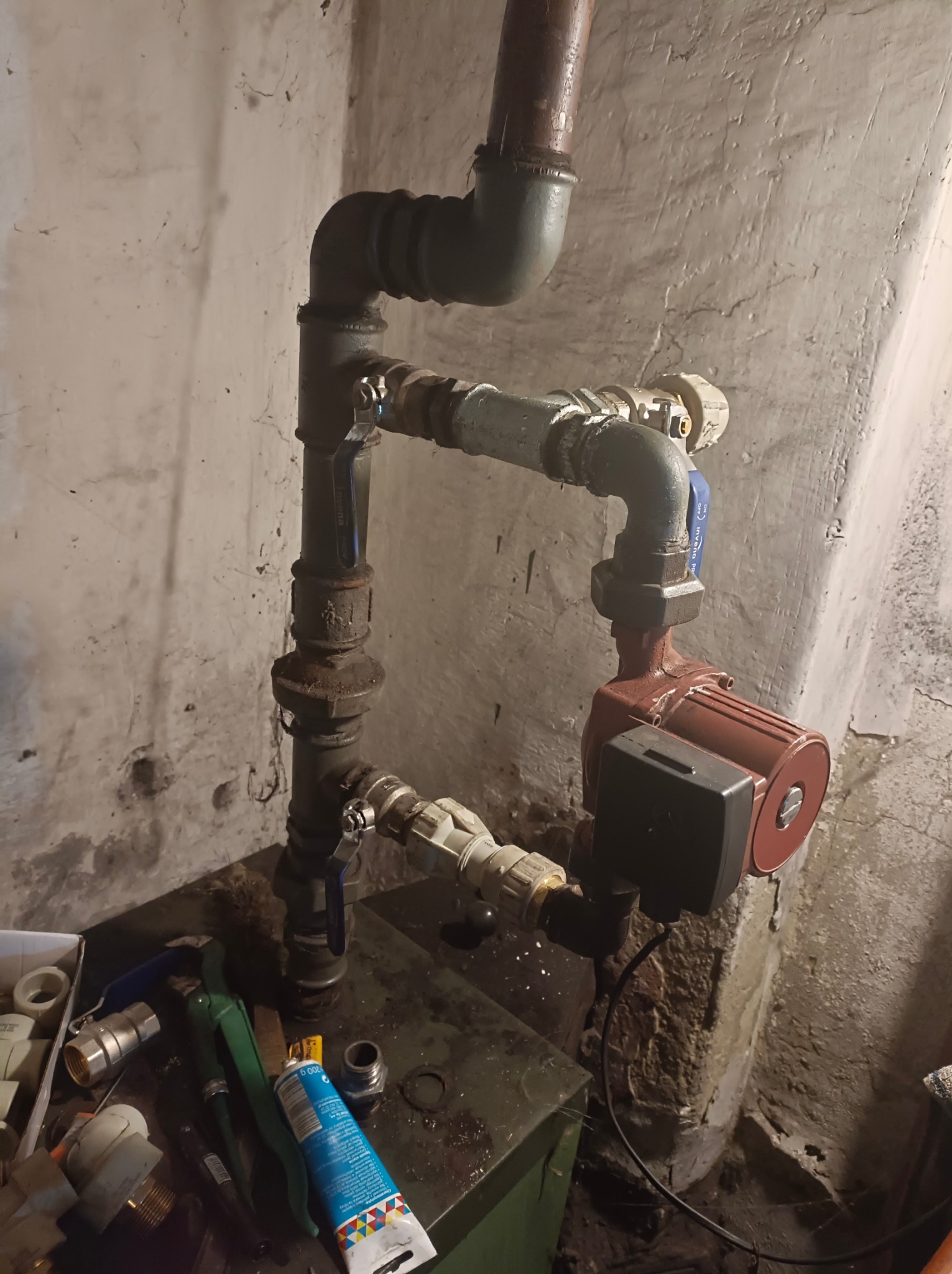 Złożona instalacja hydrauliczna z pompą obiegową, zaworami i rurami różnego typu, zamontowana w piwnicy w Pszowie, widoczne narzędzia hydrauliczne i akcesoria.