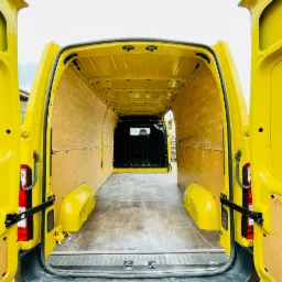 Wnętrze żółtego busa z otwartymi drzwiami, wyłożone sklejką, gotowe do załadunku.