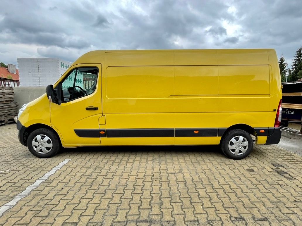 Żółty bus dostawczy Renault Master sfotografowany z boku na tle pochmurnego nieba i palet z materiałami budowlanymi.