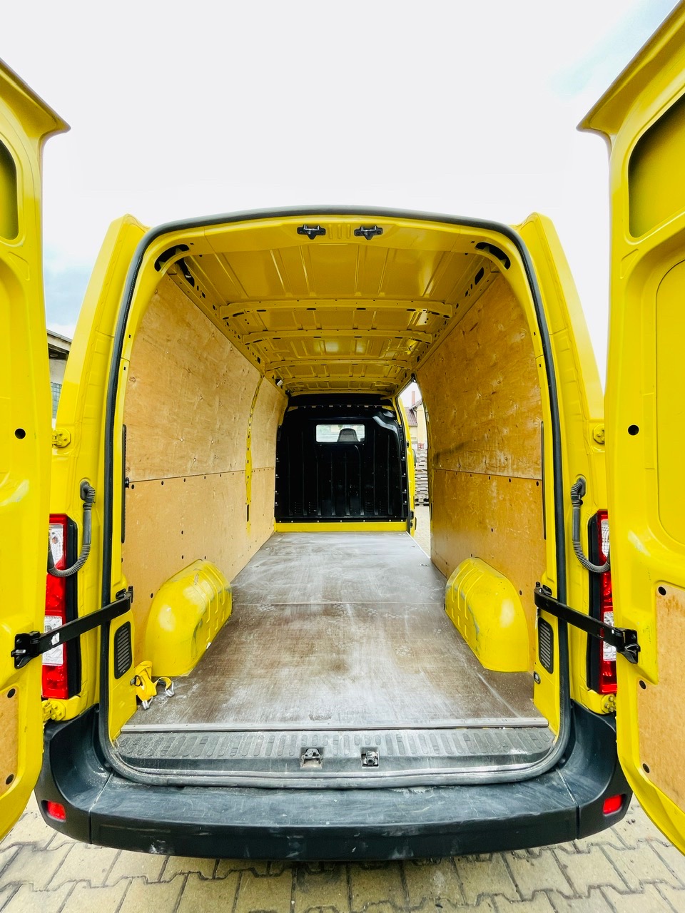 Wnętrze żółtego busa z otwartymi drzwiami, wyłożone sklejką, gotowe do załadunku.
