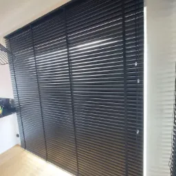 Czarne żaluzje aluminiowe zamontowane w oknie w Zambrowie, z widocznym fragmentem blatu kuchennego w tle.